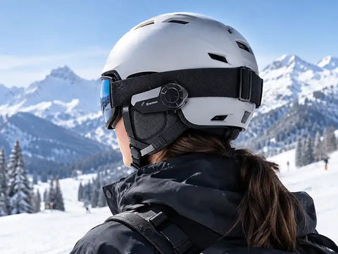 A skier wearing a helmet with a Moman intercom system, demonstrating how to communicate while skiing on snowy slopes