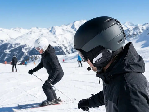 A skier wearing a helmet with a ski helmet bluetooth intercom to communicate on the slope