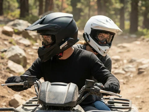 Close-up of two ATV riders wearing helmets with communication headsets riding on a dirt trail